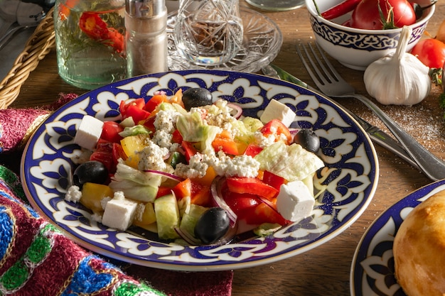 Salada grega. Salada de legumes vegetariana clássica com pimentão, pepino, cebola, azeitonas e queijo Feta, temperada com azeite em prato com padrão tradicional usbeque.
