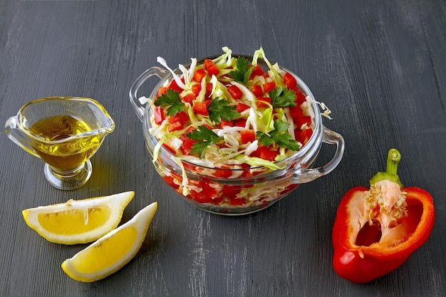 Salada leve de verão de repolho branco fresco, páprica e salsa temperada com óleo e limão em uma tigela de vidro em uma mesa de madeira preta