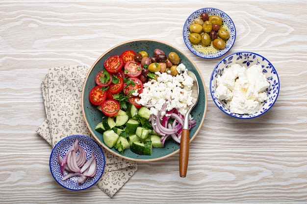 Salada mediterrânea grega com tomate, queijo feta, pepino, azeitonas inteiras e cebola roxa em prato de cerâmica azul sobre fundo branco de madeira de cima, aperitivo tradicional da Grécia
