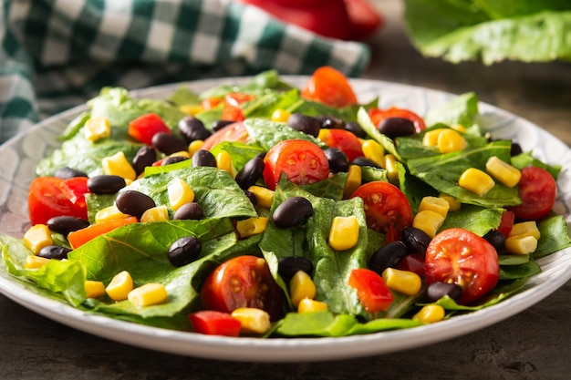 Salada mexicana com feijão preto, milho, tomate, alface e pimenta na mesa de madeira