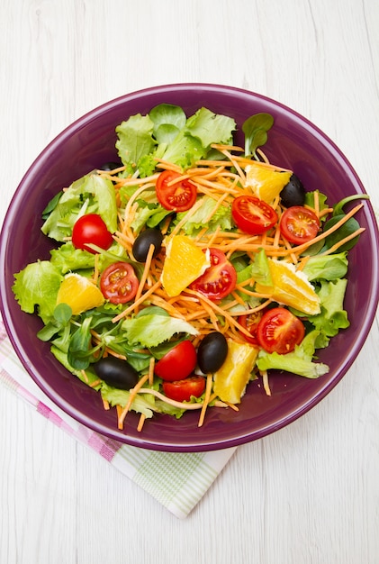 Salada mista com tomates em tigela roxa na mesa de madeira