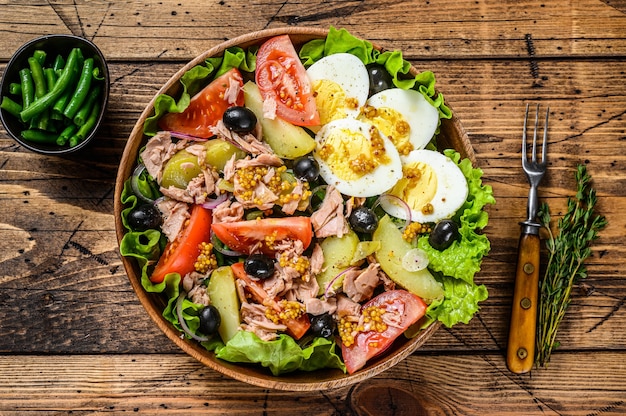 Salada Nicoise com atum, tomate, azeitonas, feijão verde, pepino, ovos cozidos e batata em uma tigela de madeira