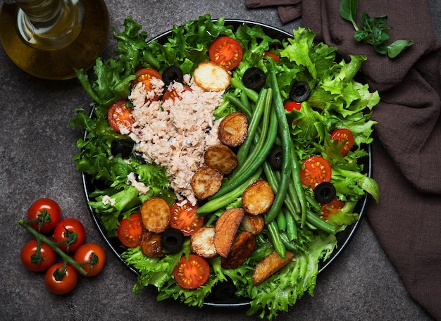 Salada Nicoise com atum, tomate, batata e feijão verde em fundo escuro, close-up