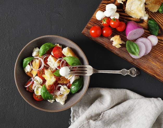 Salada panzanella italiana em uma tigela em fundo escuro com quase ingredientes