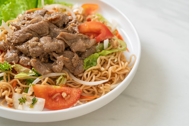 Salada picante de macarrão instantâneo com carne de porco no prato branco - comida asiática