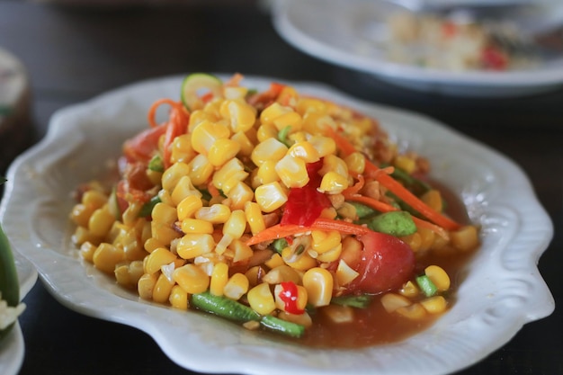 Salada picante de milho na chapa branca na mesa de madeira