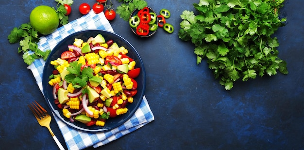 Salada picante mexicana com milho feijão vermelho abacate pimentas jalapeno tomate cereja cebola e coentro vista superior do fundo da mesa azul