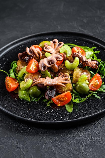 Salada quente com polvo, batatas, rúcula, tomate e azeitonas. Fundo preto. Vista do topo