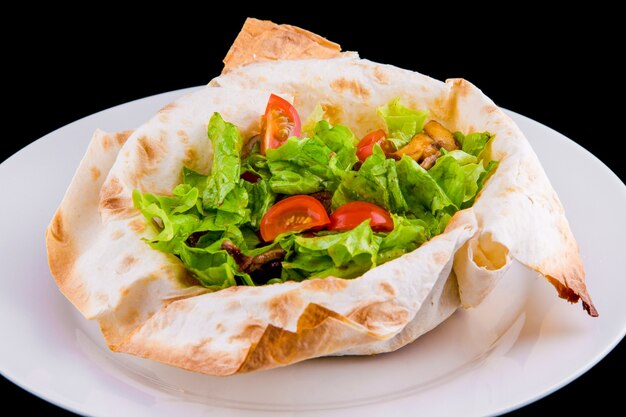 Salada quente em pão sírio fino: carne, cogumelos, tomate cereja, mostarda Dijon, conhaque. Isolado em fundo preto