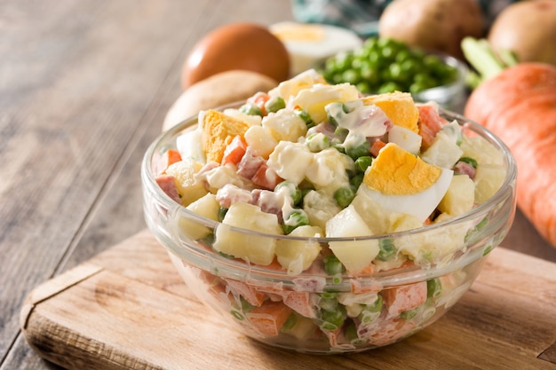 Salada russa tradicional e ingredientes, salada de olivier na mesa de madeira.