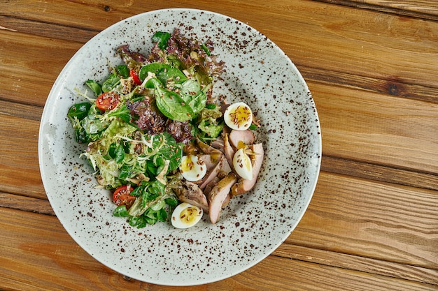 Salada saborosa e fresca com peito de pato, espinafre, quinoa, ovos de codorna e tomate cereja em uma tigela branca em uma mesa de madeira. Nutrição de fitness saudável. Fechar comida