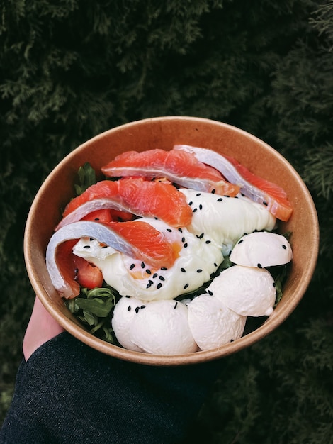 Salada saborosa saudável com ovo de salmão escalfado de rúcula em uma caixa de papelão em uma mão sobre um fundo verde de madeira. entrega de alimentos. foto de alta qualidade