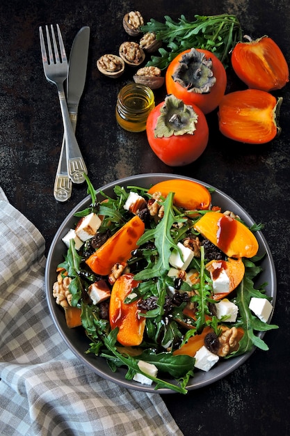 Salada saudável com caqui, rúcula, nozes e queijo feta. Comida de fitness. Superalimentos Salada de caqui de vitamina Outono.