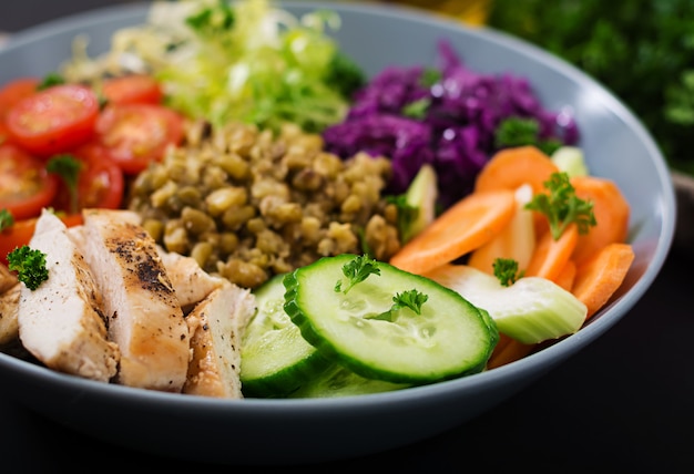 Salada saudável com frango, tomate, pepino, alface, cenoura, aipo, couve roxa e feijão mungo na mesa escura.