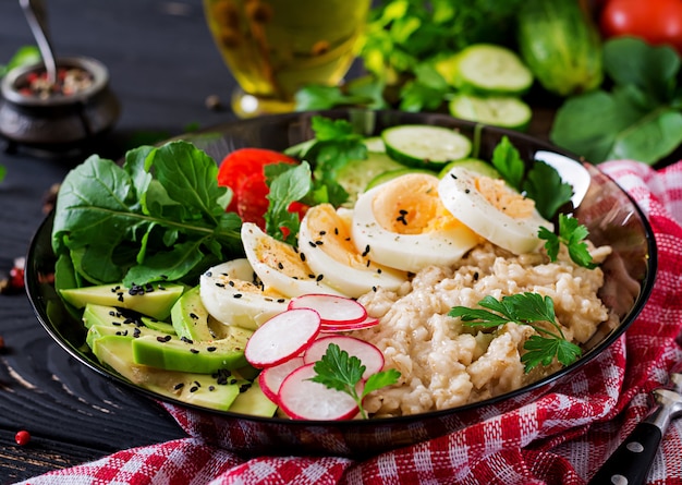 Salada saudável de legumes frescos - tomate, abacate, pepino, rabanete, ovo, rúcula e aveia na tigela. dieta alimentar.