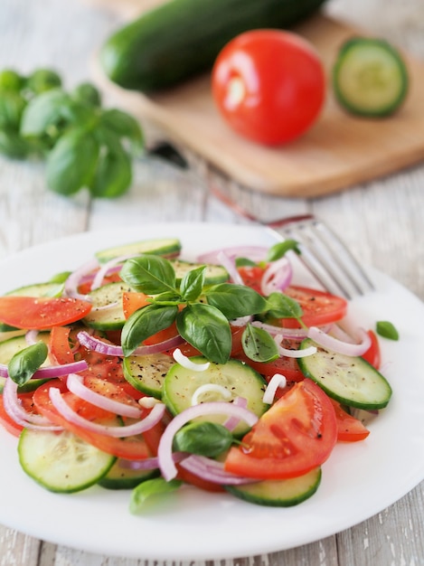 Salada saudável de tomates frescos e pepinos com manjericão em uma mesa branca rústica