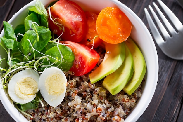 Salada saudável fresca com quinoa, tomate cereja e verduras mistas, abacate, ovo e micro verduras na madeira