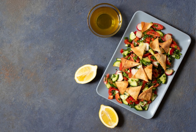 Salada tradicional de Fattoush com legumes e pão pita. Levantine, árabe, culinária do Oriente Médio. Servido em um prato retangular. Fundo escuro. Vista do topo. Espaço para texto