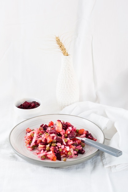 Salada tradicional russa com legumes - vinagrete e colher em um prato e uma tigela de beterraba em uma mesa em um pano. Visão vertical