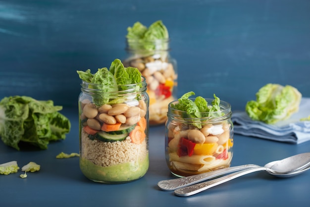 Salada vegana de cuscuz e macarrão em frascos de pedreiro com legumes feijão