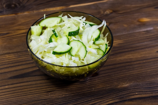 Salada vegana primavera com repolho e pepino em uma tigela de vidro na mesa de madeira