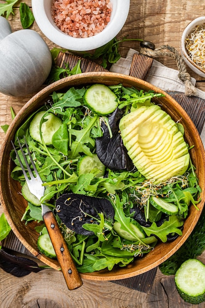 Salada vegana verde com mistura de folhas verdes, abacate e vegetais. Fundo de madeira. Vista do topo.