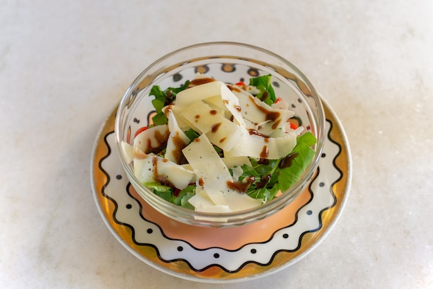 Salada vegetal verde com fatia de queijo parmesão na bacia de vidro.