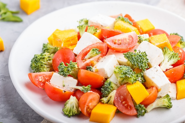 Salada vegetariana com brócolis, tomate, queijo feta e abóbora no prato de cerâmico branco