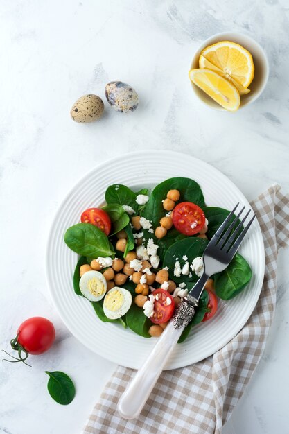 Salada vegetariana com espinafre, grão de bico, tomate cereja, ovo e queijo Feta e limão sobre um fundo claro.