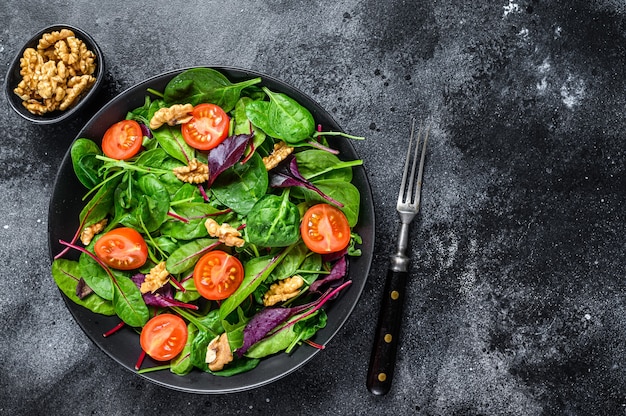 Salada vegetariana com mistura de folhas mangold, acelga, espinafre, rúcula e nozes em uma saladeira. Fundo preto. Vista do topo. Copie o espaço.