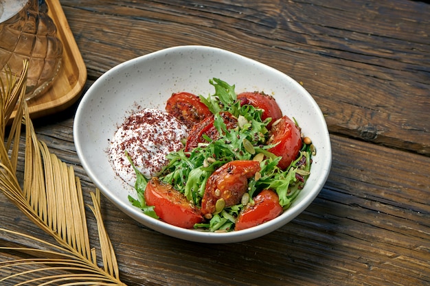 Salada vegetariana com tomates assados, iogurte grego e rúcula em uma tigela sobre uma mesa de madeira