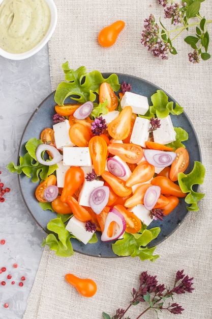 Salada vegetariana com tomates frescos de uva, queijo feta, alface e cebola na superfície de concreto cinza, vista superior.