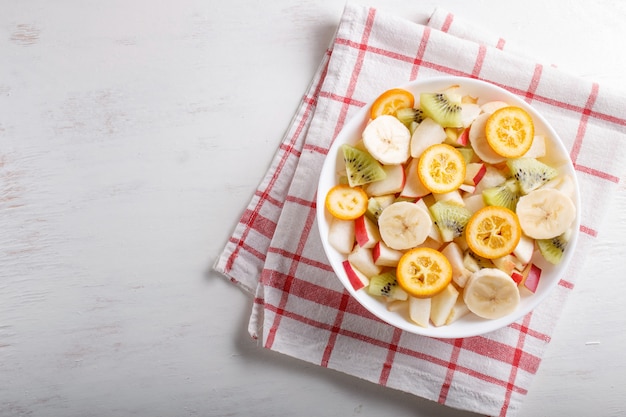 Salada vegetariana de bananas, maçãs, peras, kumquats e kiwi na toalha de mesa de linho