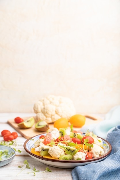 Salada vegetariana de couve-flor couve, kiwi, tomate, brotos de microgreen sobre fundo cinza de madeira. Vista lateral, foco seletivo, copie o espaço.