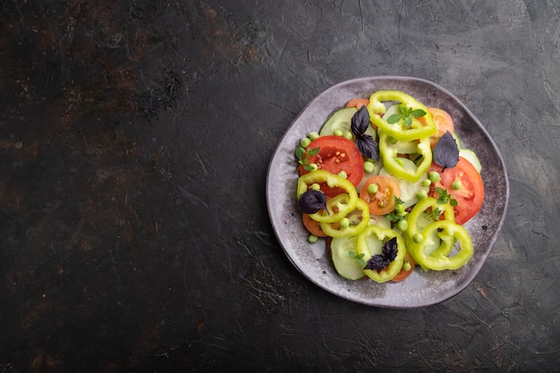 Salada vegetariana de ervilha, tomate, pimenta e manjericão em uma superfície de concreto preto