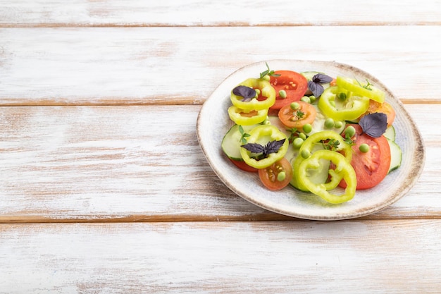 Salada vegetariana de ervilha verde tomate pimenta e manjericão no fundo branco de madeira Espaço de cópia de vista lateral