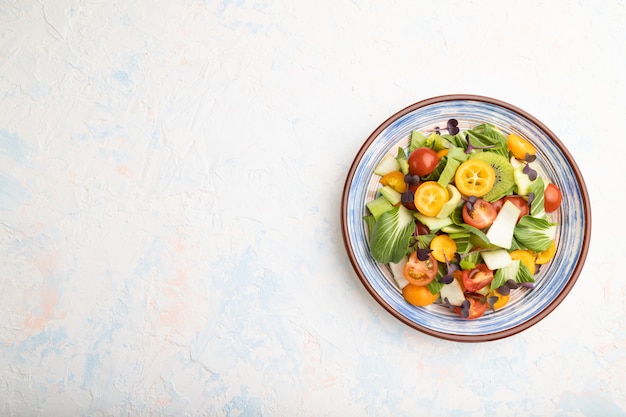 Salada vegetariana de pac choi repolho, kiwi, tomate, kumquat, microgreen brota em uma superfície de concreto branca. vista superior, copie o espaço.