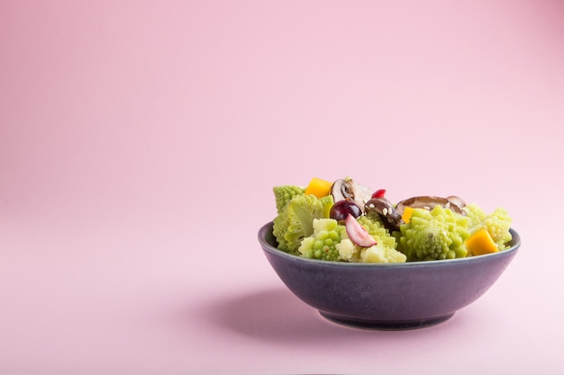 Salada vegetariana de repolho romanesco, champignon, cranberry, abacate e abóbora em um fundo rosa pastel. vista lateral, copie o espaço.