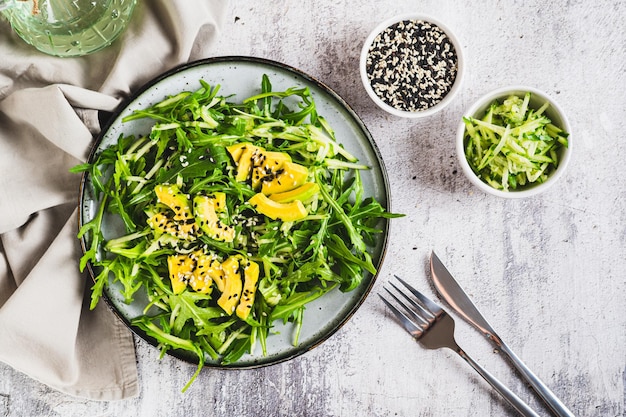 Salada vegetariana de rúcula, folhas de pepino, abacate e gergelim em um prato, vista de cima