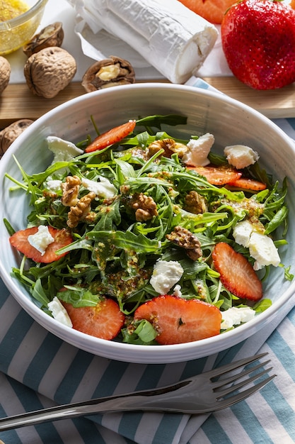 Foto salada vegetariana e saudável de rúcula verde crua e rúcula fresca, brotos e folhas de brassicaceae com morangos frescos, nozes, queijo de cabra e azeite de oliva.