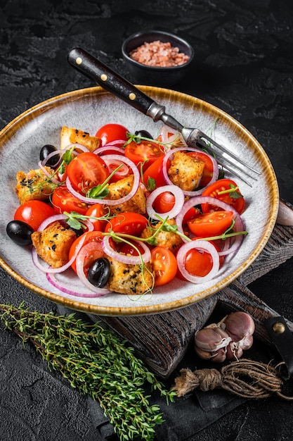 Salada vegetariana Panzanella com tomate, cebola e pão torrado. Fundo preto. Vista do topo.