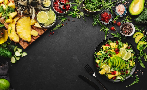 Salada vegetariana vegana com abacaxi rúcula, abacate e cereja seca na chapa preta na vista superior da mesa de cozinha de pedra escura alimentação saudável dieta limpa conceito de perda de peso