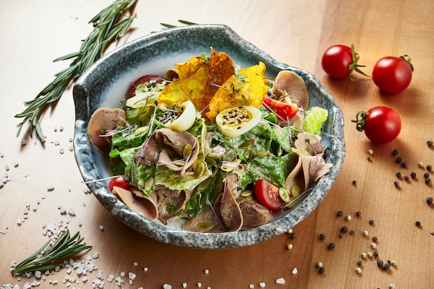 Salada verde com alface, língua de vitela assada em uma tigela branca sobre uma superfície de madeira em uma composição com especiarias