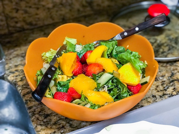 Salada verde com manga e morango na tigela.