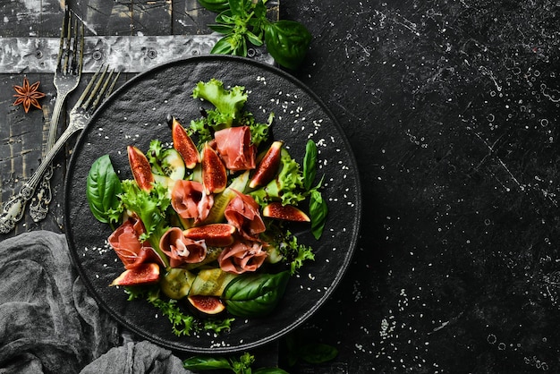 Salada verde com pepino presunto e figo em uma placa de pedra preta Comida Vista superior Espaço livre para o seu texto