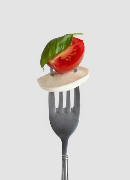 salada verde com tomate e mussarela em um garfo em um fundo branco