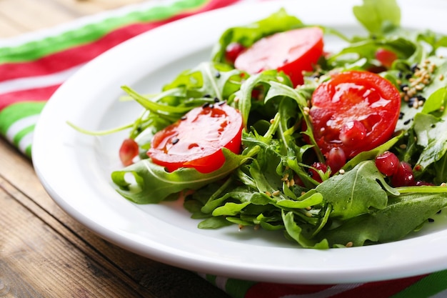 Salada verde feita com tomate rúcula e gergelim no prato sobre fundo de madeira