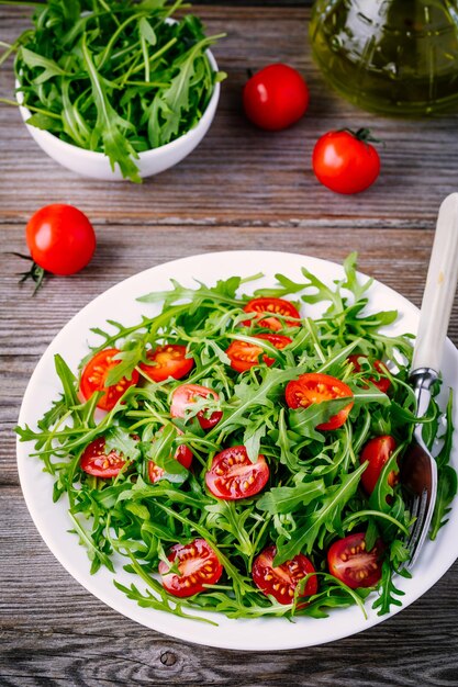 Salada verde fresca com rúcula e tomate vermelho sobre fundo de madeira rústico