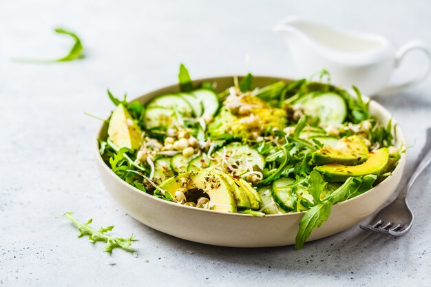 Salada verde saudável com abacate, pepino e rúcula no prato branco.