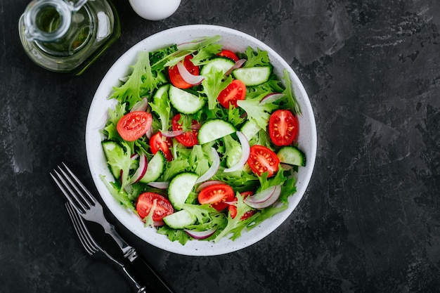 Salada verde saudável com tomate fresco pepino cebola vermelha e alface em tigela sobre fundo escuro de pedra espaço de cópia de vista superior